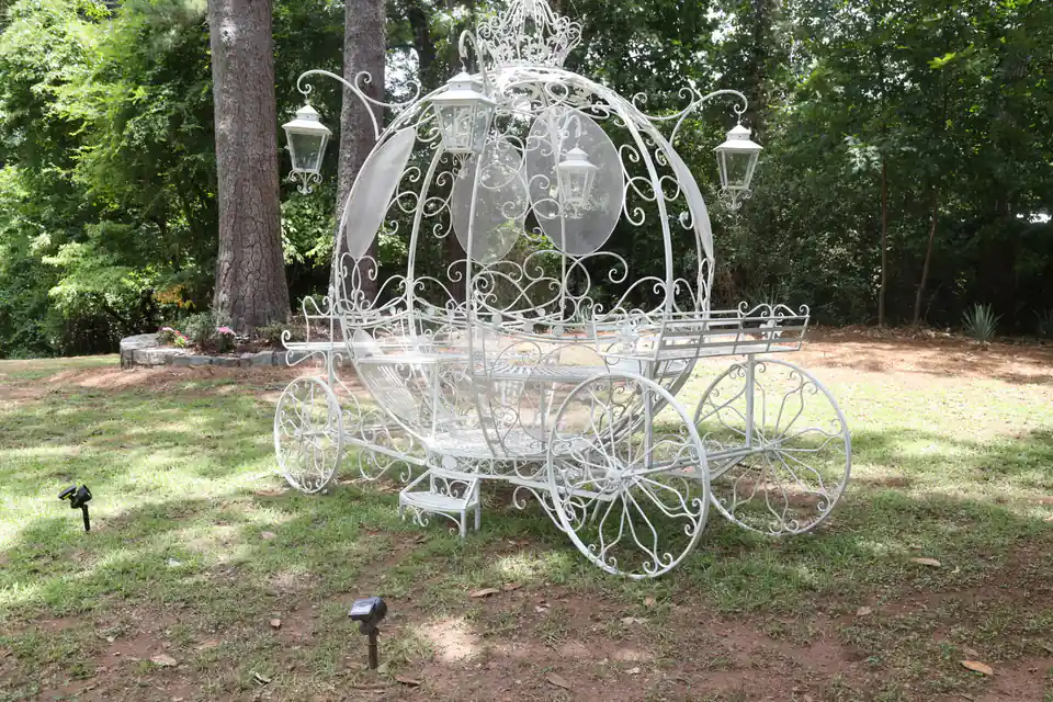 A white wrought-iron carriage standing among the trees