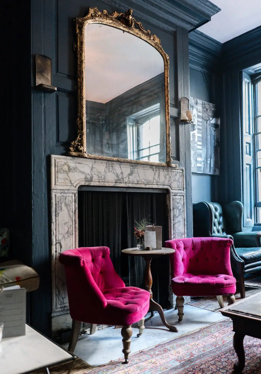 A lounge with a gilded mirror, marble fireplace and velvet chairs